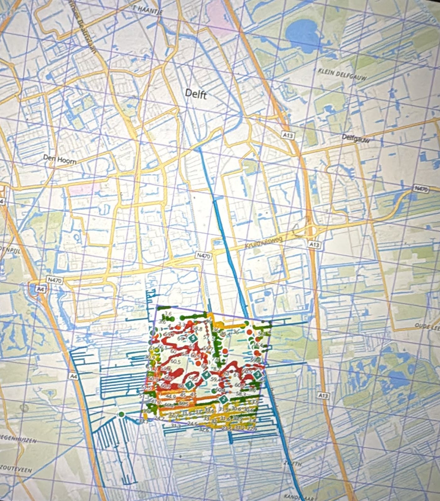 A map of the area around Delft in the Netherlands with a simulated tile overlaid. Within the tile, waterways are marked with coloured points and numeric suitability scores running from green through orange to red.